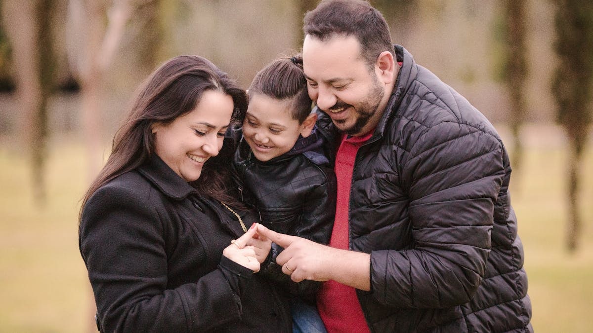 A joyful family of three enjoys a tender moment outdoors, depicting warmth and love.