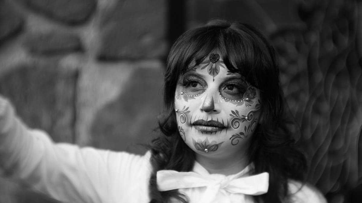 Mexican woman with skull makeup celebrating Dia de los Muertos outdoors in grayscale.
